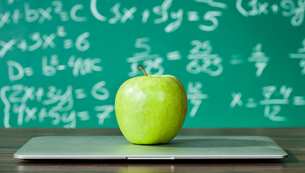Laptop and apple in front of chalk board