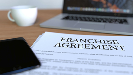 Franchise Agreement papers with phone, coffee and laptop